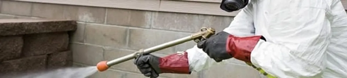 Pest control technician applying exterior insect treatment along a home foundation in Cedar Rapids, IA