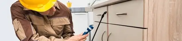 Roach exterminator applying treatment under kitchen cabinets in Cedar Rapids, IA