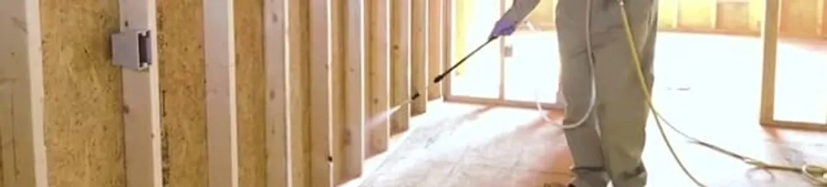 Termite treatment technician applying spray along framing and unfinished walls in Cedar Rapids, IA