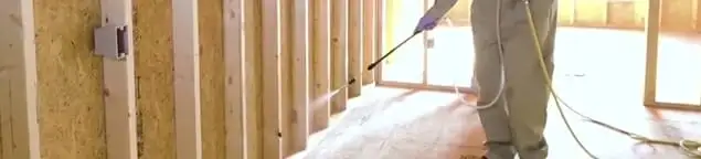Termite treatment technician applying spray along framing and unfinished walls in Cedar Rapids, IA